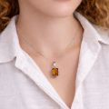 Woman wearing genuine Baltic amber rectangular pendant necklace in 925 sterling silver on delicate chain, close-up lifestyle jewelry photo